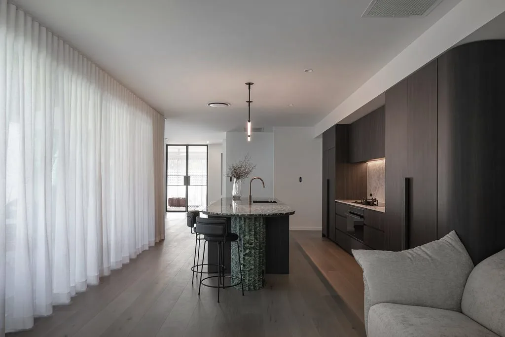 Long open room with sheer curtains and dark kitchen joinery, Noir House