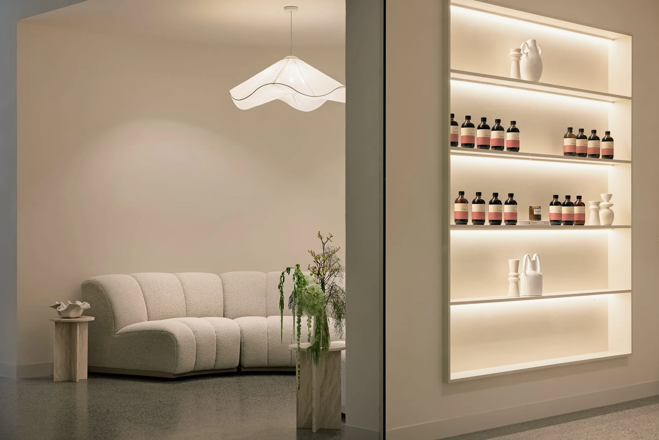 Curved cream sofa beside lit shelves of bottles, Ritual Haus